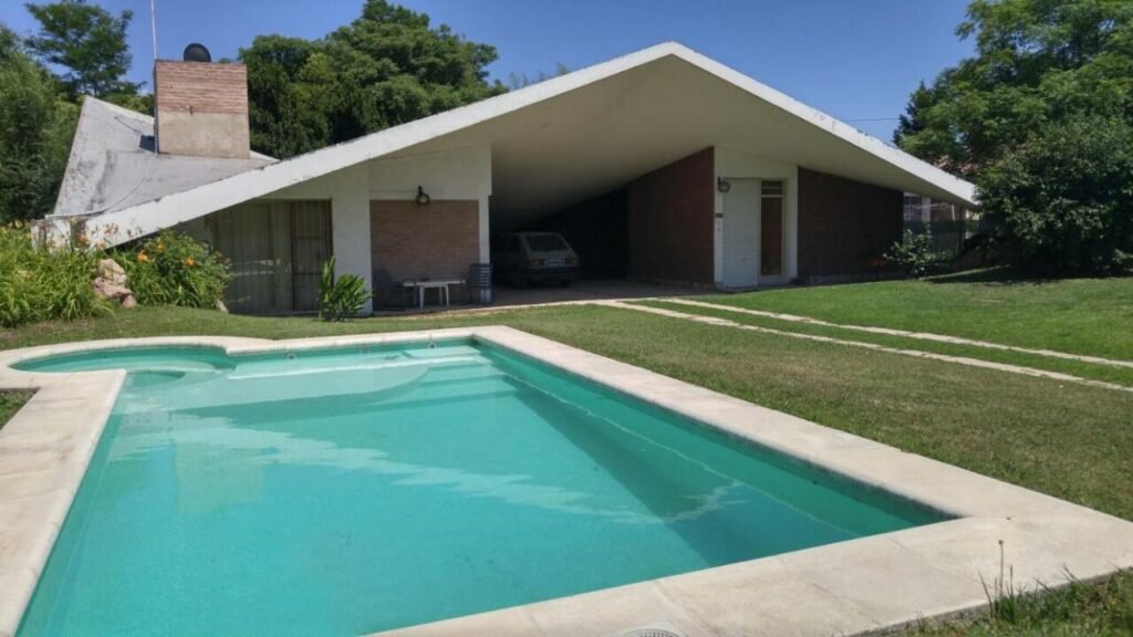 Pileta con solado y parque, con la casa de fondo, en un alquiler temporario de Villa Carlos Paz